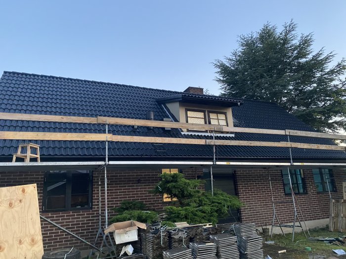 Nyrenoverat tak på hus med takpannor, takfönster och ventilationsutrustning, stöttas av byggställning.