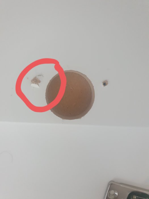Felaktigt gängad skruvhål i vit vägg markerad med röd cirkel, nära beslag och brunt område.