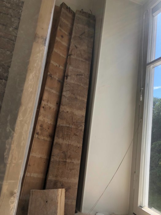 Tjocka träplankor lutade mot en vägg intill ett fönster.