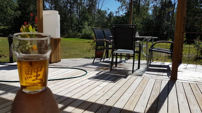 Ett glas öl i förgrunden med en suddig utsikt över en solig terrass och trädgårdsmöbler i bakgrunden.