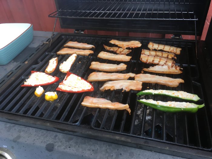 Grillat kött och fyllda paprikor/chili på en gasolgrill, med en skål i bakgrunden.