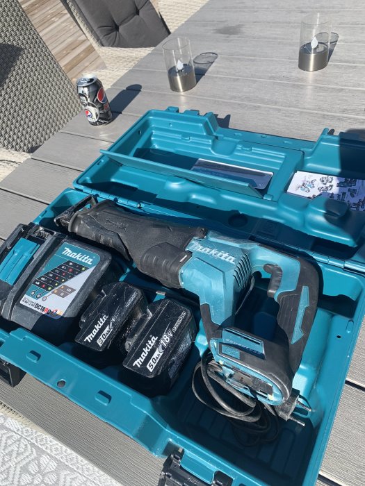 Begagnad Makita tigersåg DJR187RTE med batterier i blå väska, på ett träbord utomhus.