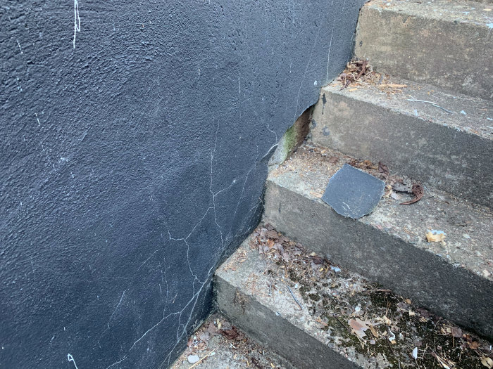 Yttervägg med svart puts och sprickor som lossnat på en källartrappa, synlig luftspalt och skador.