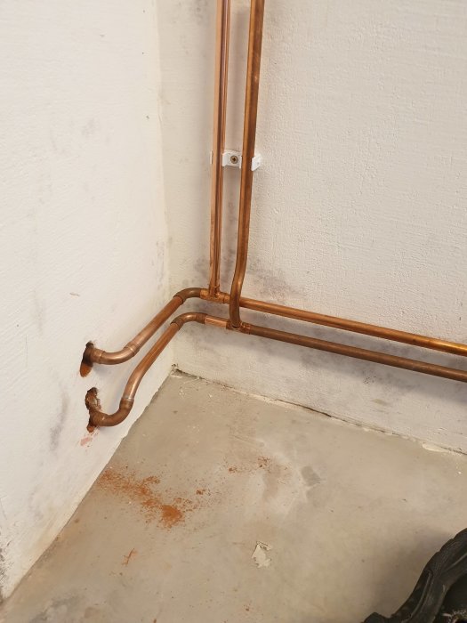 Nyligen sammanfogade kopparrör för radiatorinstallation i ett källarutrymme.