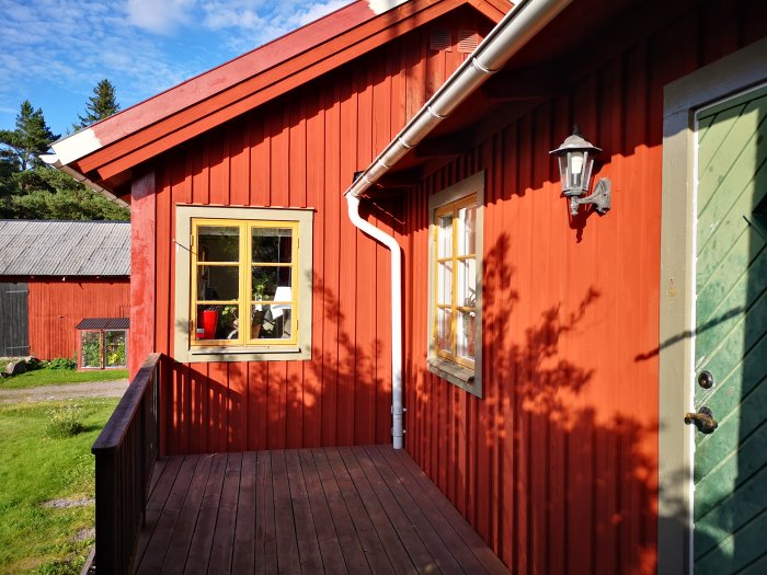 Ny målning på husvägg med Falu rödfärg, solbelyst veranda och skuggor av grenar.