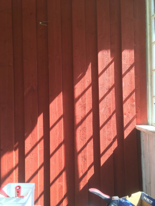 Schackrutigt mönster av skuggor på rödfärgad vägg med ett soligt fönster som ljuskälla.
