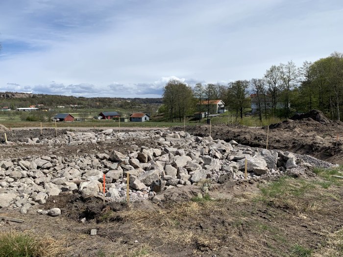 Utlagda stora stenar på en byggplats med gräsmark och hus i bakgrunden.