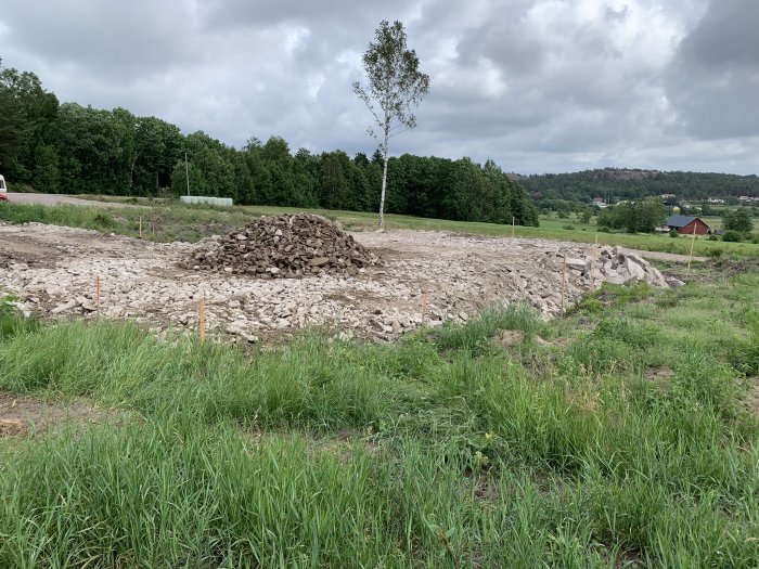 Byggarbetsplats med en stor hög av sten och grus redo för vältning i grönt landskap.