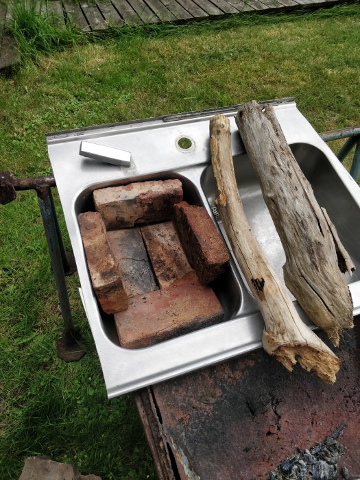 Äldre diskho återanvänds som arbetsyta med tegelstenar och ved, placerad utomhus på en rostig metallstruktur.