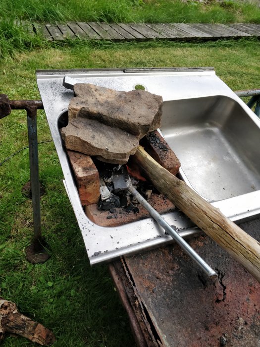 Improviserad utekök med en överbliven diskho använd som eldstad för matlagning, stående på rostiga bockar.