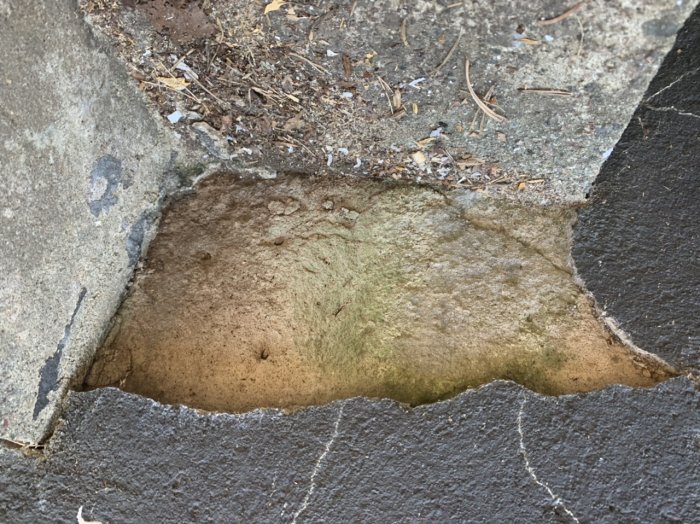 Bild av en trasig betongkant mot jorden, synlig skada och smuts, orienterad uppochner.