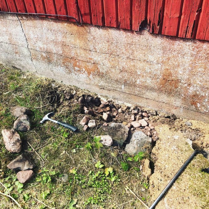 Renoveringsarbete vid husgrund där sten och puts har grävts fram med hacka på marken.