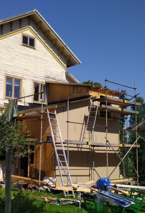 Hus under renovering med väderskyddat nedre tak, byggnadsställningar och en stege.