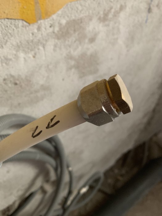 Slutet av en pex-rörledning med en metallkoppling mot en betongvägg.