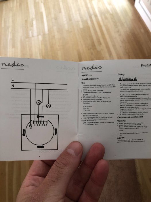 Hand håller upp en öppen manual med ett kopplingsschema för smart ljusstyrning, inkluderande strömbrytare och ledningar.