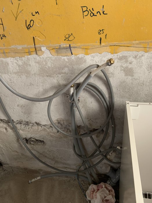 Vattenledningar och anslutningsrör ligger på ett oorganiserat sätt mot en vägg med anteckningar.