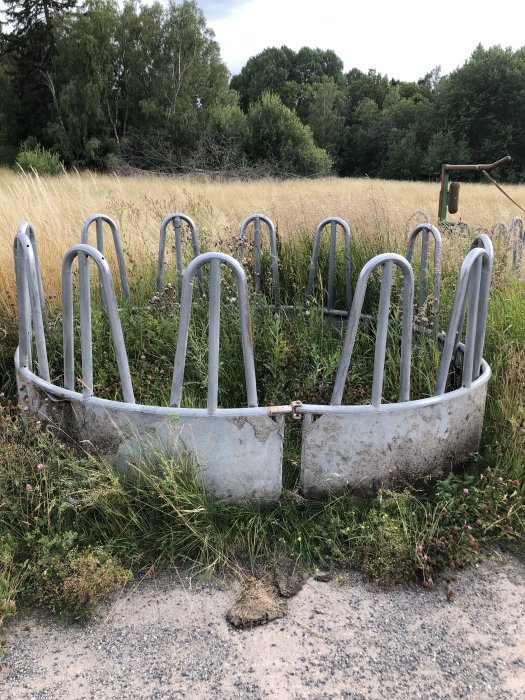 Halvfärdig foderhage av varmförzinkade stålrör placerad på grus med skog och gräs i bakgrunden.