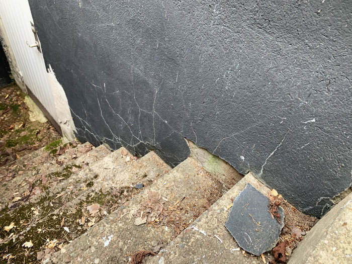 Vägg med vita sprickor intill en trappa som tyder på potentiella fuktproblem i källaren.