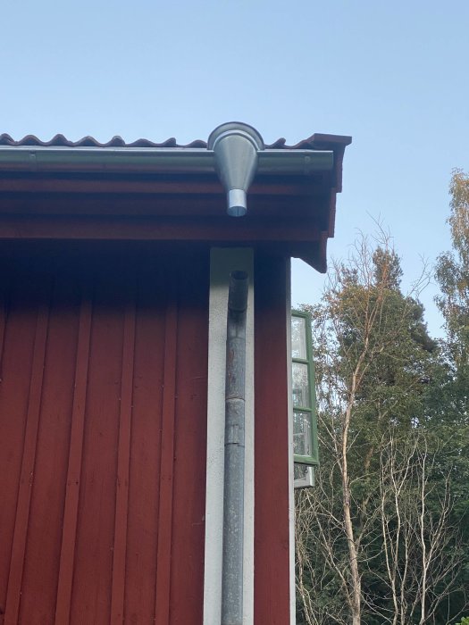 Nyinstallerade handgjorda rännor och vattkupa på ett rött trähus med plåttak.