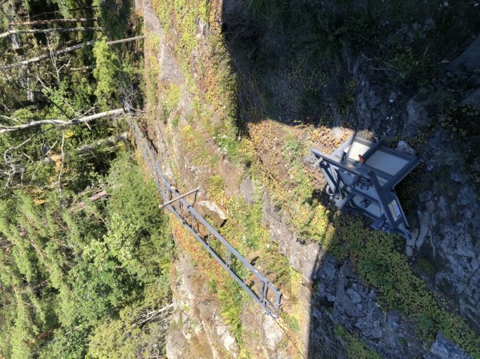 En delvis installerad järnvägsräls på en sluttande skogsterräng med stolpskor och en byggnadsutrustning.