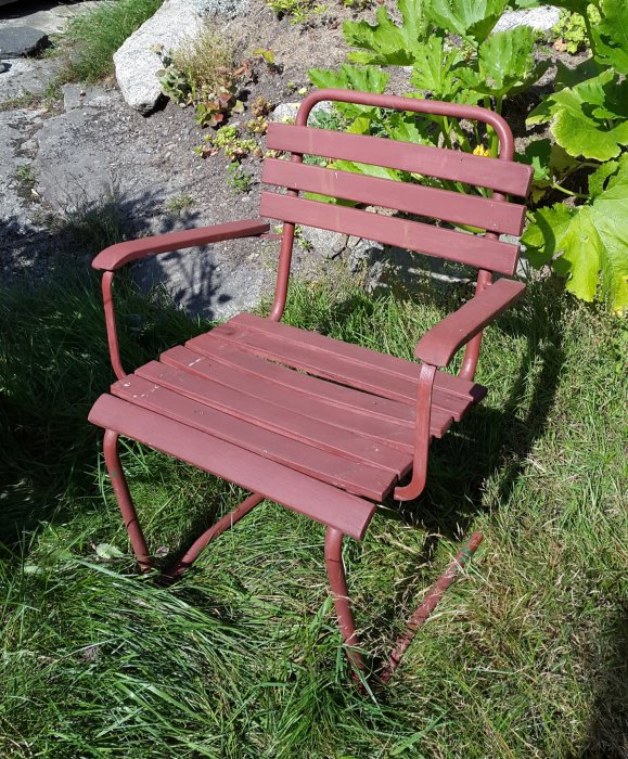 Röd, klassisk gungstol av stålram i en trädgård, vanlig från 50-talet till 70-talet.