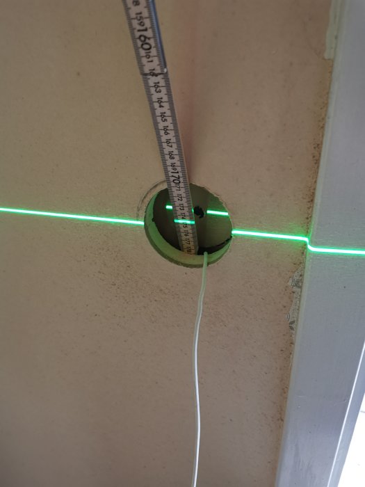 Installation av vägguttag med laserlinje, meterstock och dragtråd genom isoleringen.