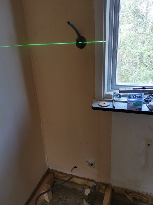 Lasernivå som projicerar en grön linje för installation av vägguttag i ett renoveringskök.