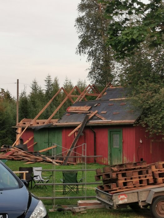 Renoveringsarbete på röd ekonomibyggnad med avtäckt tak och byggnadsställning.