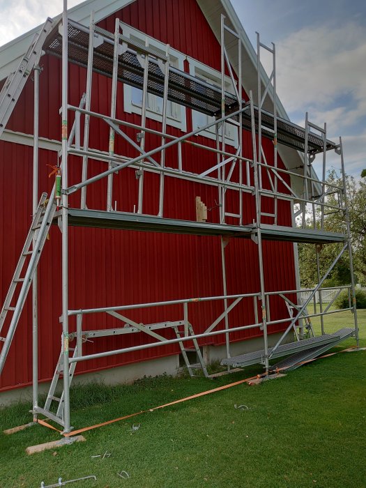 Ställning monterad mot en röd vägg på ett rött hus, antyder förberedelse för yttre arbete.