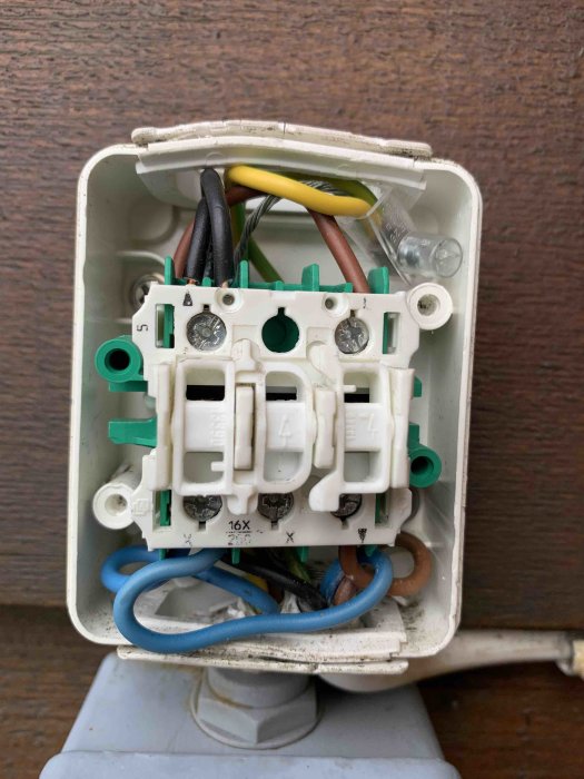 En gammal sliten strömbrytare öppnad uppvisar anslutna kablar och skruvterminaler, behov av utbyte.