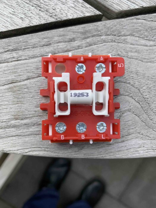 Översiktsbild av en röd och vit elströmbrytare som hålls i handen, med synliga skruvanslutningar och modellnummer.