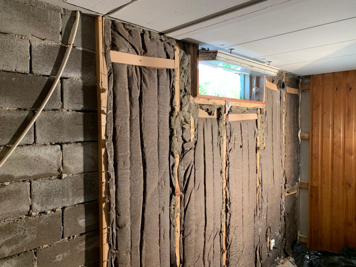Rivet väggparti under renovering visar isolering med träfibrer mellan träreglar och bakomliggande betongblock.