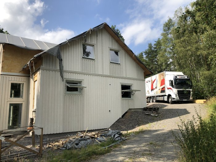 Halv-isolerat hus med öppen vägg och isoleringsmaterial, bredvid en lastbil.