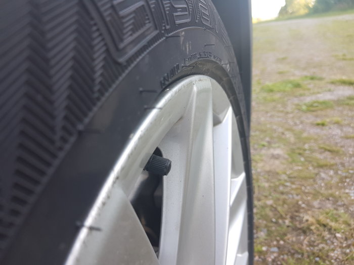Närbild på bilens däck som sticker ut från fälgen, vilket ifrågasätts av bilägaren.