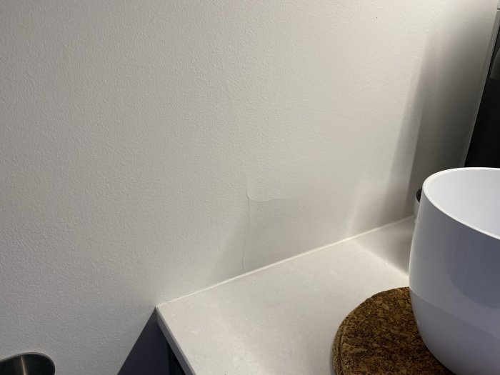 Spricka i en målad tapet ovanför en diskbänk i ett kök, sprickan är synlig på kortsidan av väggen.