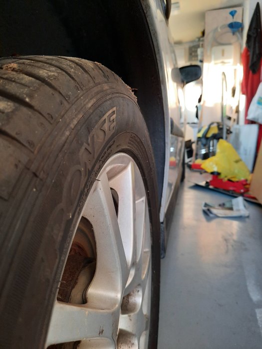 Närbild på ett slitaget bilhjul med synlig fälgräddarkant i ett garage.