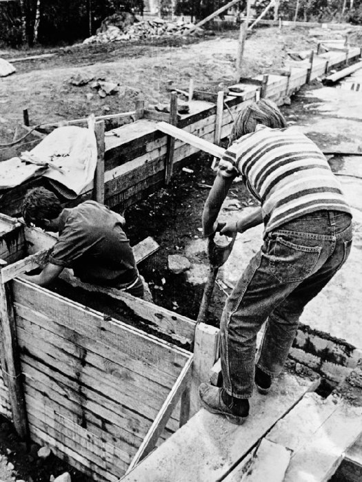 Svartvit bild från 1969 som visar två personer som bygger grundläggningen för ett hus.