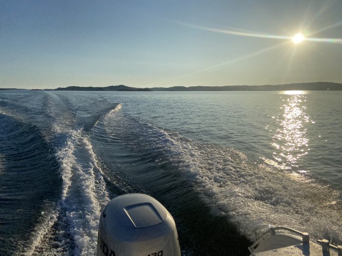 Solnedgång vid havet med båtmotor och vaken i förgrunden, vy från en båt.