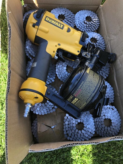 Fabriksrenoverad Dewalt D51321 spikpistol och en låda av 21 mm pappspik på rulle i gräset.