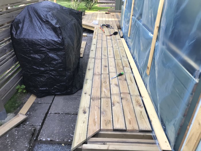 Åldrad obehandlad trall under renovering med verktyg utspridda på den nyvända ytan bredvid en grillöverdrag.