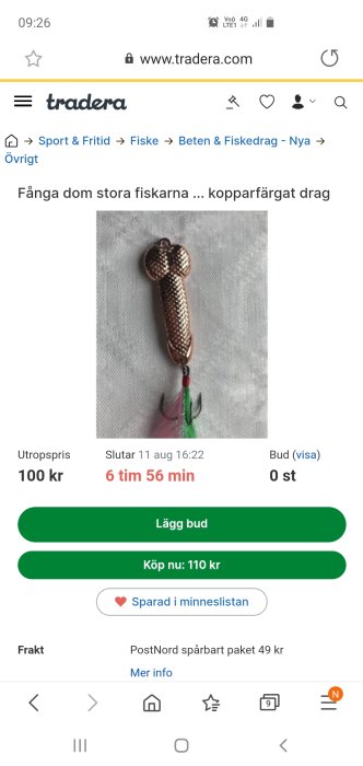 Kopparfärgat fiskedrag med krokar och gröna samt rosa detaljer på en vit bakgrund.