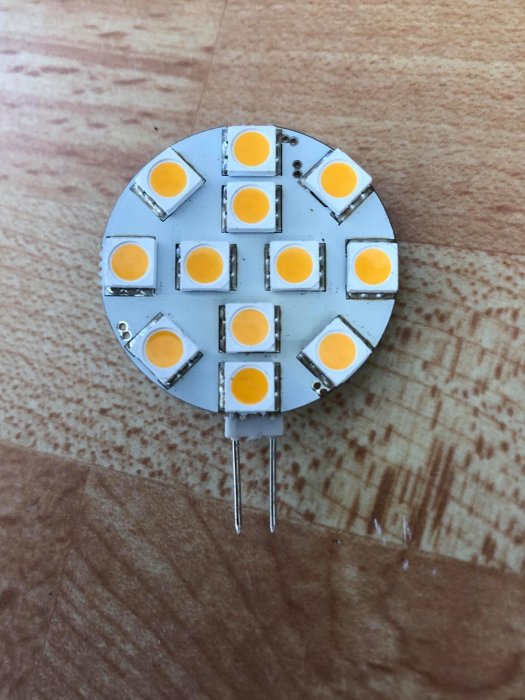 LED-lampa med G4-sockel och flera dioder på ett träunderlag.