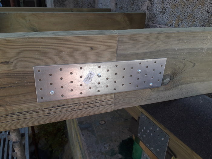 Två grova träbjälkar sammanfogade med en metallplatta och skruvar i byggprojekt.