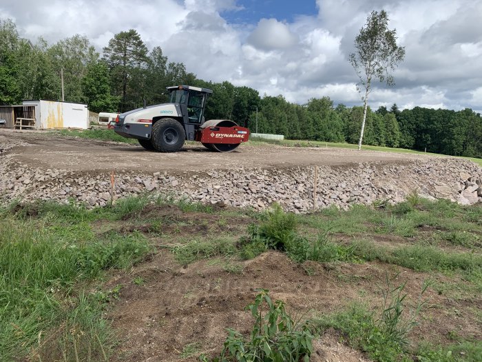 Vältmaskin på en byggplats med nyligen packat gruslager och utsättningspinnar i marken.