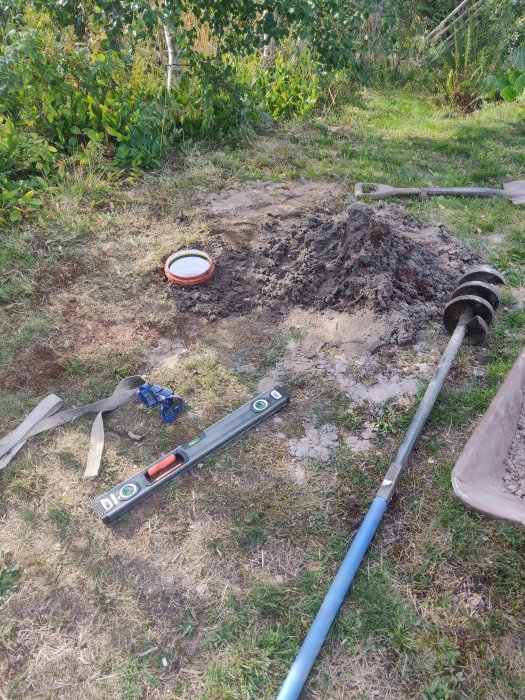 Grävd grop i trädgården med foderrör, spade, vattenpass och borr för brunnsborrning, 230 cm djupt.