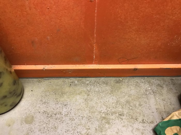 Nyisolerad vägg med orange färg vid betonggolv i garagedel, visar isoleringsdetaljer.