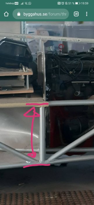 Ritad pil på bild anger höjden på ett metallramverk i en verkstad med diverse utrustning i bakgrunden.
