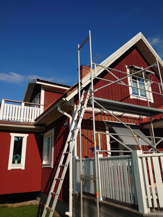 Renovering av övre vindskiva på röd trävilla, stegar och byggställning uppställda.