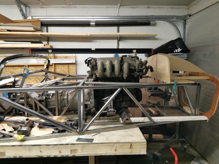 Bild på fordonram i verkstad med monterad motor och provisorisk kartongmodell av fordonets nos och instrumentpanel.
