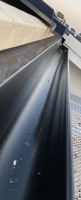 Snedbild av svart takavvattningssystem och underliggande träläkt vid huskant.